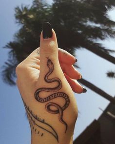 a woman's hand with a snake tattoo on her left arm and palm trees in the background