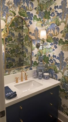 a bathroom with blue and white wallpaper, gold faucet sink and mirror