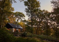 a small cabin in the woods with trees around it and a fenced in area