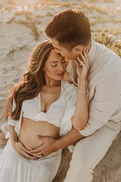 a pregnant couple cuddling on the beach