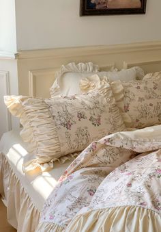 a bed with ruffled sheets and pillows on top of it next to a painting