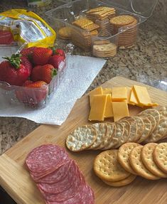 a wooden cutting board topped with cheese and crackers next to strawberries on a counter