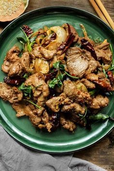 a green plate topped with meat and veggies next to chopsticks on a wooden table