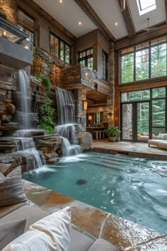 a large indoor swimming pool with waterfall and seating area next to the water feature, surrounded by windows