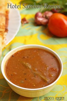 there is a bowl of soup on the table next to some pita bread and tomatoes