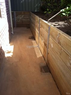 a wooden fence next to a brick wall and green plants on the side of it