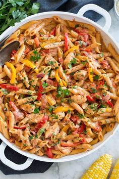 a skillet filled with pasta, chicken and peppers on top of a marble counter