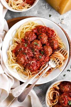 two bowls of spaghetti with meatballs and parmesan cheese on the side next to bread