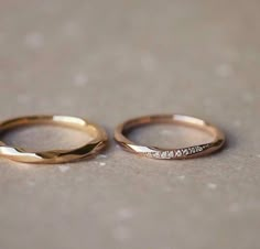 two gold wedding rings sitting on top of a cement floor next to eachother