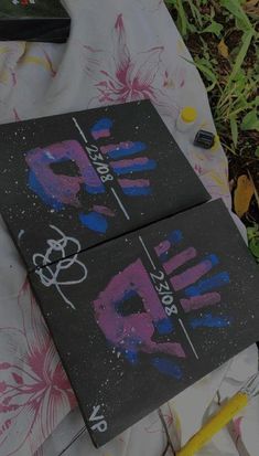 two pieces of black paper with pink and blue paint on them sitting on a blanket