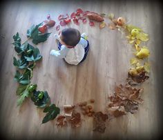 a toddler sitting on the floor surrounded by leaves and other autumn things that are scattered around him