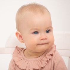 a close up of a baby wearing a pink shirt and smiling at the camera while sitting on a white chair