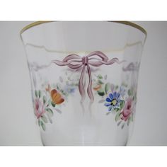 a glass vase with flowers painted on the side and a ribbon tied around it's edge