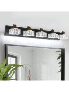 a bathroom vanity with three lights and a mirror on the wall next to a potted plant