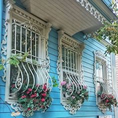 three windows with flowers in them on the side of a blue house