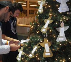 two men are decorating a christmas tree with paper angel decorations on it while another man is looking at his cell phone