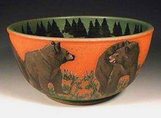 an orange and green bowl with bears painted on the side, in front of trees