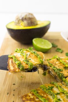 a wooden cutting board topped with slices of pizza covered in green sauce and toppings