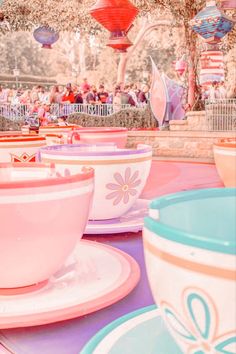 many colorful cups and saucers are on display at the amusement park with people in the background