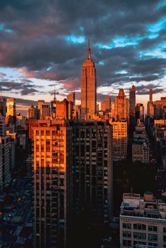 the city skyline is lit up at sunset with clouds in the sky and buildings on either side