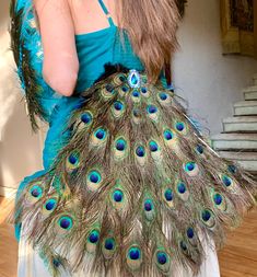 a woman in a blue dress holding a peacock feather purse with feathers all over her body