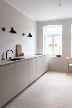 an empty kitchen with white cabinets and black lights on the windowsill, along with wooden flooring