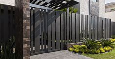 a modern gate in front of a house with plants and flowers on the side walk