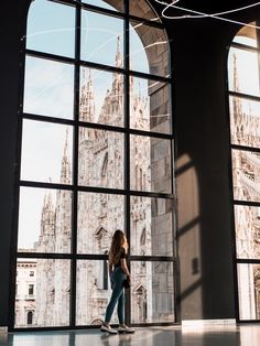 a woman standing in front of a large window looking out at the cathedral and clock tower