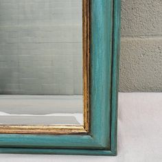 a blue and gold framed mirror sitting on top of a white table next to a brick wall