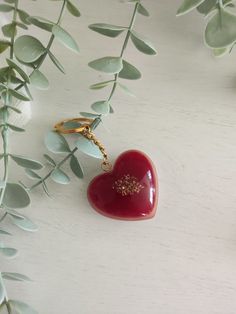 a red heart shaped keychain sitting on top of a white table next to green leaves