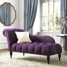 a purple chair sitting in front of a window next to a table with flowers on it