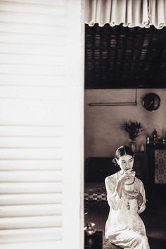 an old photo of a woman sitting on a chair holding a cup in her hand