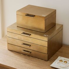 two gold boxes sitting on top of a wooden table next to a pearl necklace box