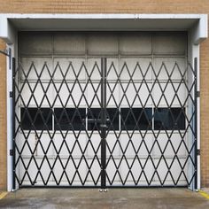 an open garage door with black bars on the side and white walls behind it, in front of a brick building