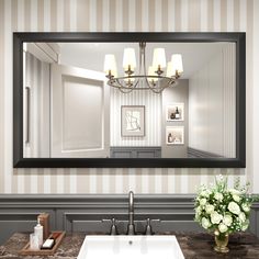 a bathroom sink sitting under a large mirror next to a vase with flowers on it