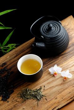 a cup of tea next to some flowers on a cutting board with a teapot