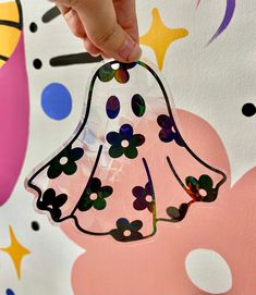 a hand holding a plastic bell ornament in front of a colorful background