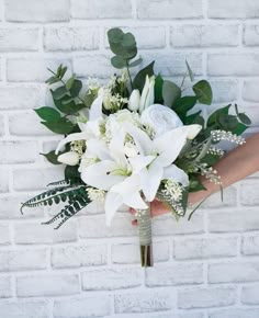 a bridal bouquet with white flowers and greenery in front of a brick wall