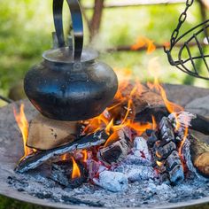 a kettle sitting on top of a fire pit filled with wood and burning coals