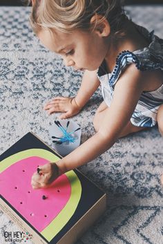 a toddler playing with a watermelon cutout on the floor in front of a box