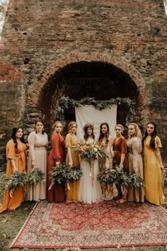 a group of women standing next to each other in front of a brick wall with greenery