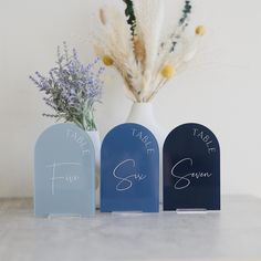 three vases with flowers in them sitting on a table next to some fake plants