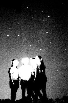 black and white photograph of three people standing on the beach at night with stars in the sky