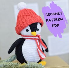 a crocheted penguin with a red hat and scarf sitting on top of a cardboard box