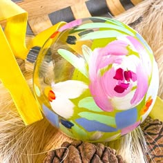 an ornament with flowers on it sitting next to some pine cones and yellow ribbon