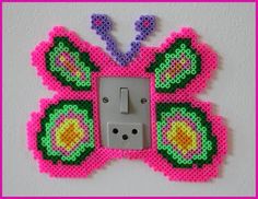 a pink and green butterfly shaped light switch cover on a white wall with a pink frame