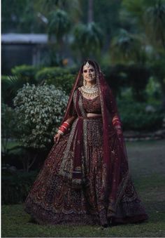 a woman in a red and gold bridal gown standing on grass with trees behind her