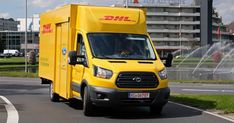 a yellow dhl delivery truck driving down the road with water spouting in the background