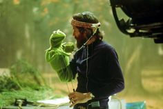 a man holding a kermie the frog puppet in front of a camera and recording equipment