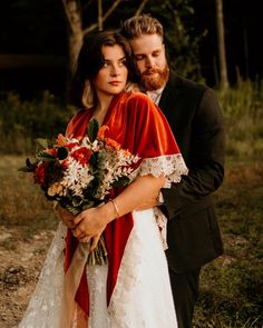 a man and woman standing next to each other in front of some trees holding flowers